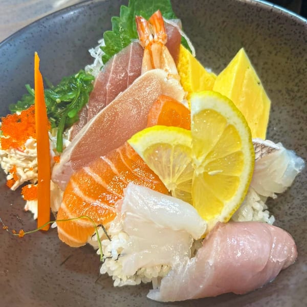 A colorful Hachi sushi & omakase chirashi bowl with various fish, shrimp, egg, and lemon slices.