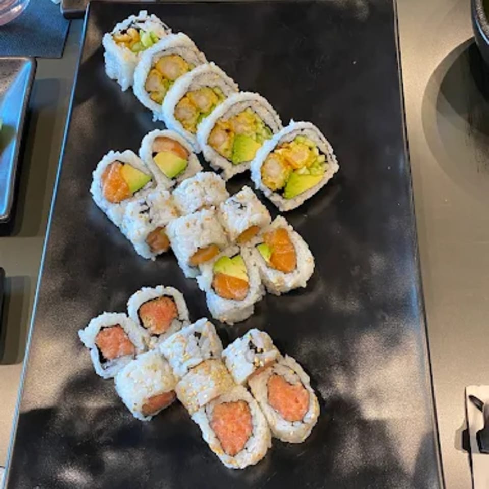 Assortment of Hachi sushi rolls with salmon, avocado, and shrimp tempura on a black platter.