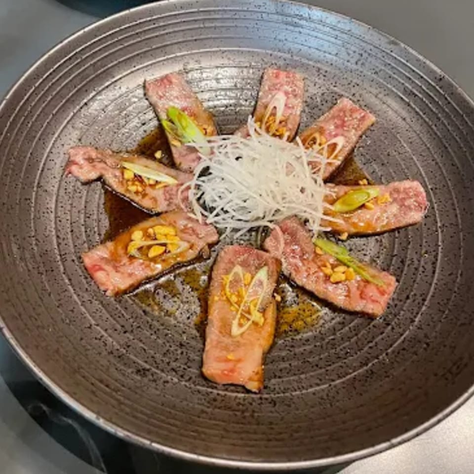 Seared wagyu beef slices with sauce, garlic chips, and shredded daikon radish on a dark plate.