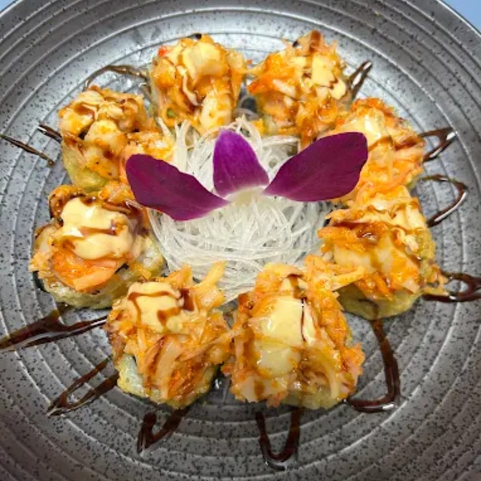 Hachi sushi rolls with creamy topping and dark sauce, garnished with a purple orchid on a gray plate.