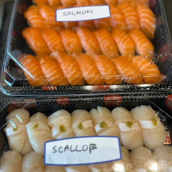Two plastic containers of Hachi sushi, one with salmon nigiri and the other with scallop nigiri.