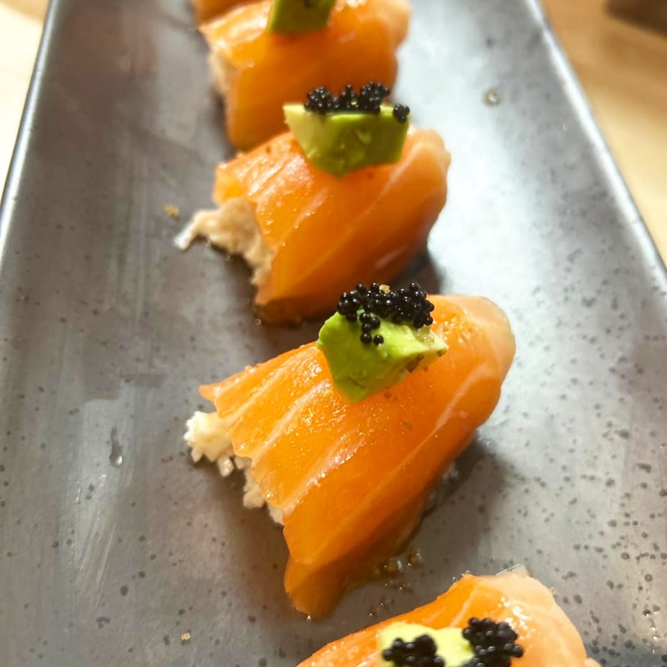 Hachi sushi & omakase salmon nigiri with avocado and black caviar on a dark plate.