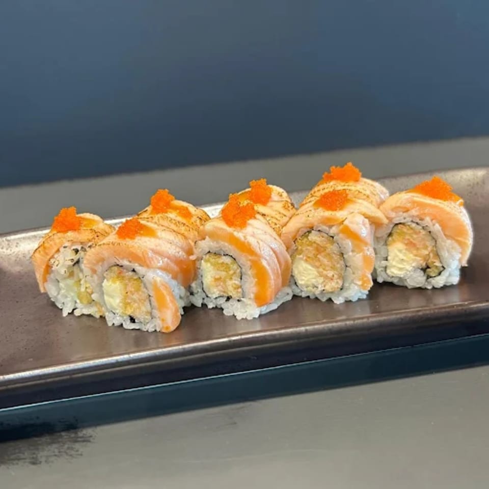 Five pieces of Hachi sushi with salmon, rice, and orange roe on a dark rectangular plate.